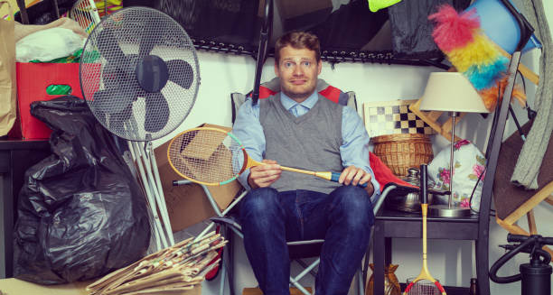 Man surrounded by clutter and household items in a hoarded room