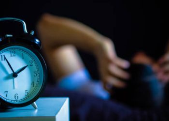 Alarm clock at 3 a.m. with a person lying awake in the background