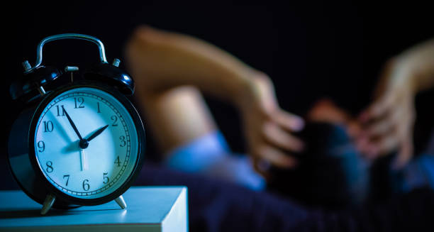 Alarm clock at 3 a.m. with a person lying awake in the background