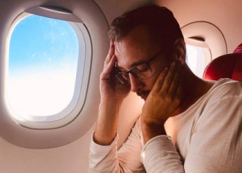 Man experiencing exhaustion and discomfort on an airplane, showing complications of jet lag