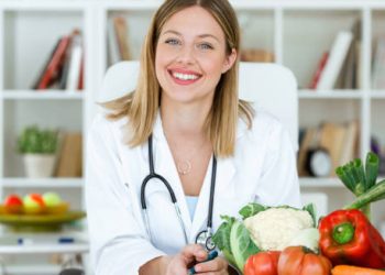 Smiling nutritionist with fresh vegetables on desk