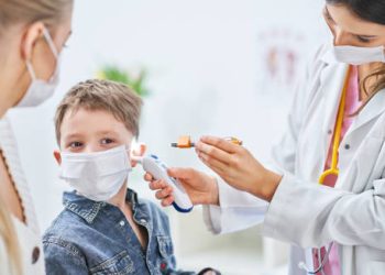 Doctor examining young boy's ear for signs of glue ear during a clinical assessment