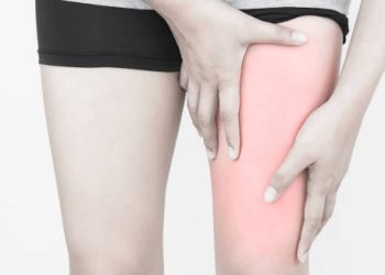 Person holding upper thigh with visible redness, indicating hamstring pain or muscle strain