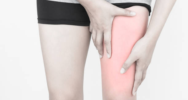 Person holding upper thigh with visible redness, indicating hamstring pain or muscle strain