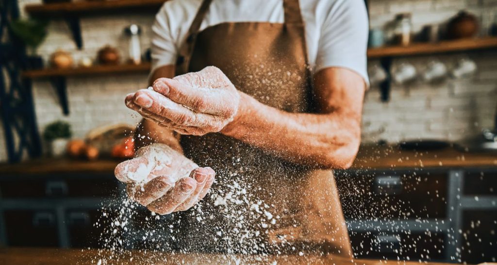 Baker clapping flour-covered hands in a kitchen, symbolising action and courage