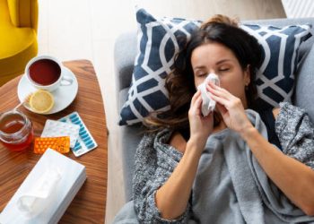 Sick woman lying on couch using tissue for flu symptoms