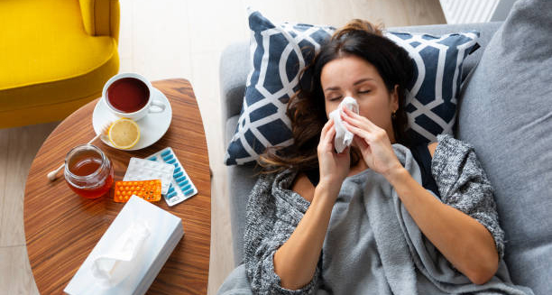 Sick woman lying on couch using tissue for flu symptoms