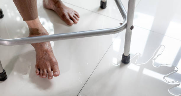 Elderly person with foot drop using a walker beside a puddle on the floor