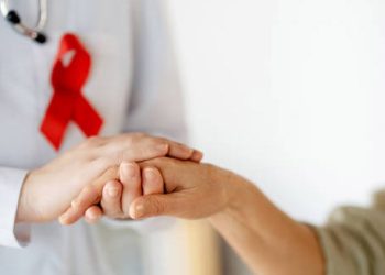 Doctor with red HIV awareness ribbon holding a patient's hand