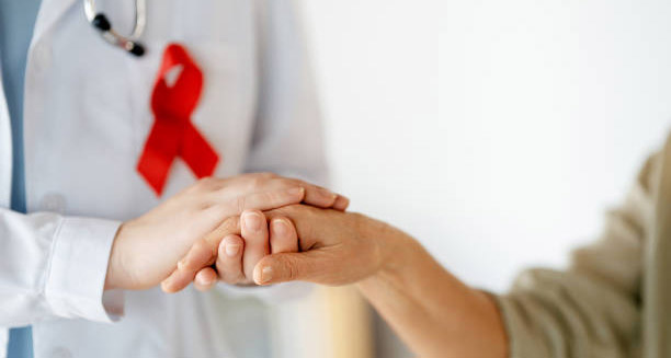 Doctor with red HIV awareness ribbon holding a patient's hand