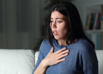 Worried woman clutching chest with anxious expression on sofa