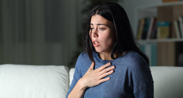 Worried woman clutching chest with anxious expression on sofa