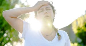Overheated woman holding her forehead outdoors, showing symptoms of heat exhaustion