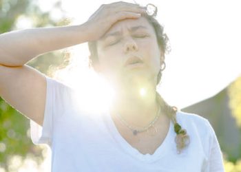 Overheated woman holding her forehead outdoors, showing symptoms of heat exhaustion