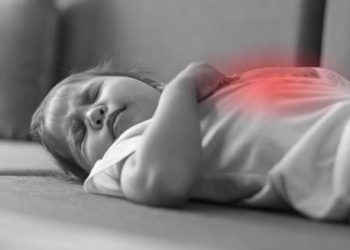 Sick toddler lying on couch clutching abdomen in pain