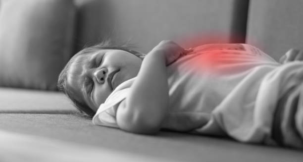 Sick toddler lying on couch clutching abdomen in pain