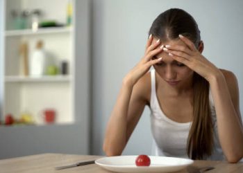 Young woman with no appetite staring at a plate with a single tomato, showing signs of iron deficiency anaemia