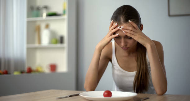Young woman with no appetite staring at a plate with a single tomato, showing signs of iron deficiency anaemia