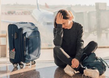 Tired traveller sitting on the airport floor with luggage, showing signs of jet lag