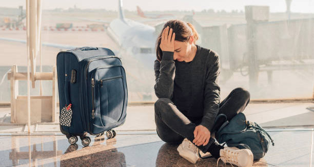 Tired traveller sitting on the airport floor with luggage, showing signs of jet lag
