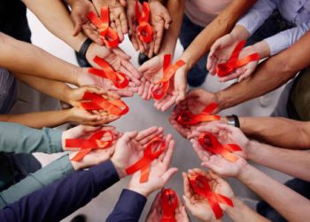 Group of hands holding red HIV awareness ribbons in unity