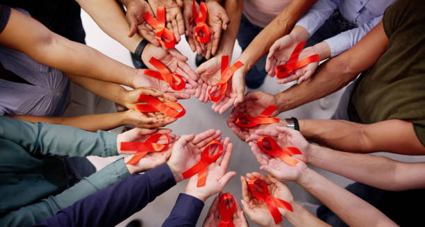 Group of hands holding red HIV awareness ribbons in unity