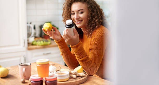 Smiling woman holding supplements and lemon, surrounded by natural remedies in kitchen