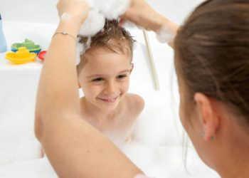 Mother washing young boy’s hair in a bubbly bath as part of lice prevention routine