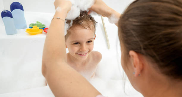 Mother washing young boy’s hair in a bubbly bath as part of lice prevention routine