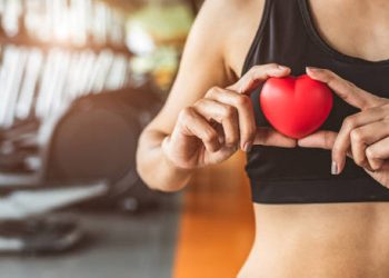 Fit woman holding red heart-shaped model in gym environment