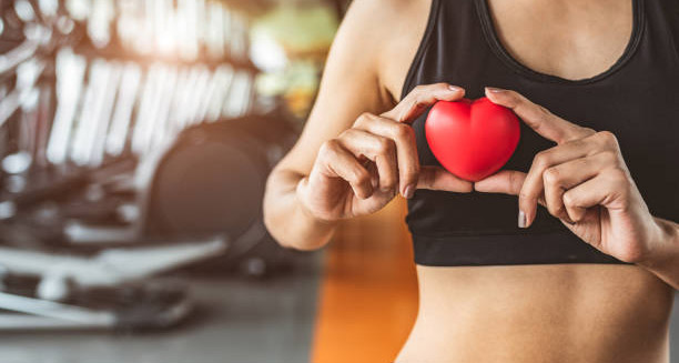 Fit woman holding red heart-shaped model in gym environment