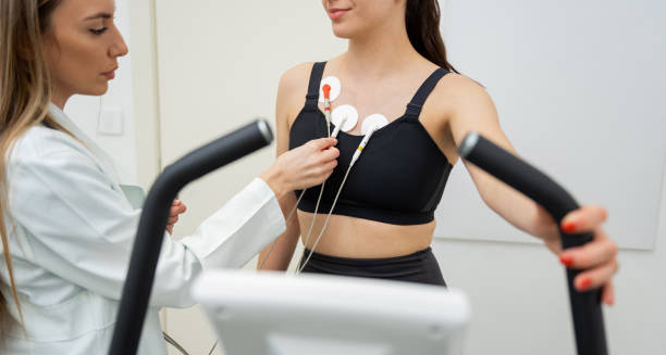 Doctor attaching ECG electrodes to a woman during treadmill test for heart block monitoring