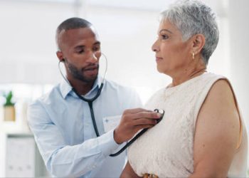 Doctor listening to elderly woman’s chest with stethoscope during heart health check-up