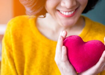 Smiling woman holding a red heart-shaped object, symbolising positive heart health outlook