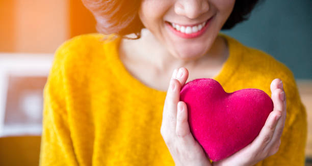 Smiling woman holding a red heart-shaped object, symbolising positive heart health outlook