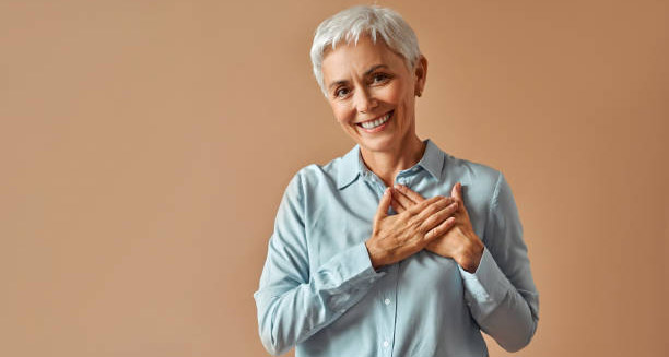 Smiling elderly woman holding her hands over her heart, symbolising positive heart health outcomes