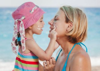 Child applying sunscreen to her mother’s face at the beach, representing a positive outlook for heat rash prevention