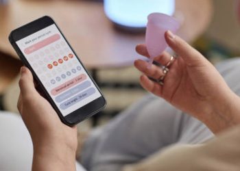 Person using a menstrual tracking app while holding a menstrual cup