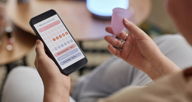 Person using a menstrual tracking app while holding a menstrual cup
