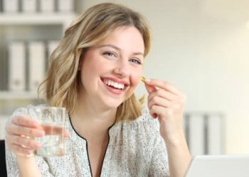Smiling woman holding a pill and water, representing positive outlook for Hepatitis C treatment