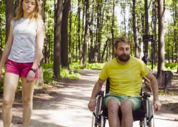 Man in wheelchair and woman walking in forest, reflecting life with hereditary spastic paraplegia
