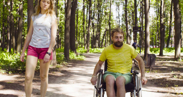 Man in wheelchair and woman walking in forest, reflecting life with hereditary spastic paraplegia