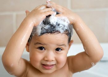 Smiling child washing hair with shampoo in a bath as part of head lice prevention