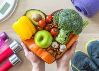 Heart-shaped bowl filled with healthy foods surrounded by fitness equipment for heart failure prevention