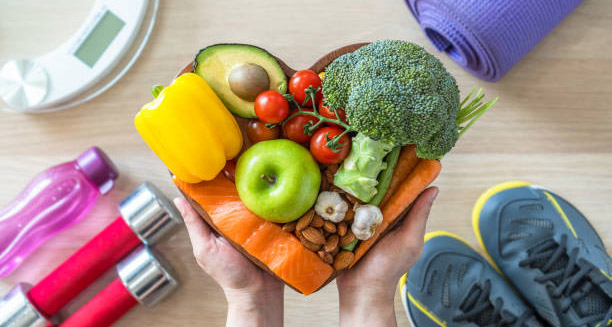 Heart-shaped bowl filled with healthy foods surrounded by fitness equipment for heart failure prevention