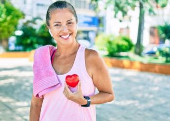 Smiling woman holding a red heart shape after exercise to promote heart health