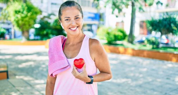 Smiling woman holding a red heart shape after exercise to promote heart health