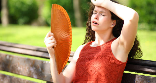 Woman sitting on a bench using a fan to cool down and prevent heat exhaustion