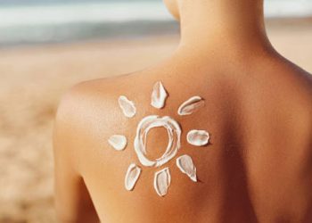 Woman on beach with sun cream in the shape of a sun on her back, symbolising prevention of heat rash