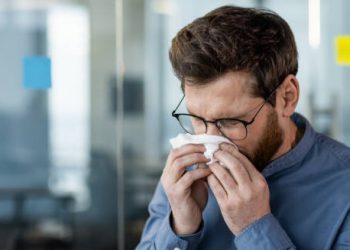 Man sneezing into tissue showing flu symptoms
